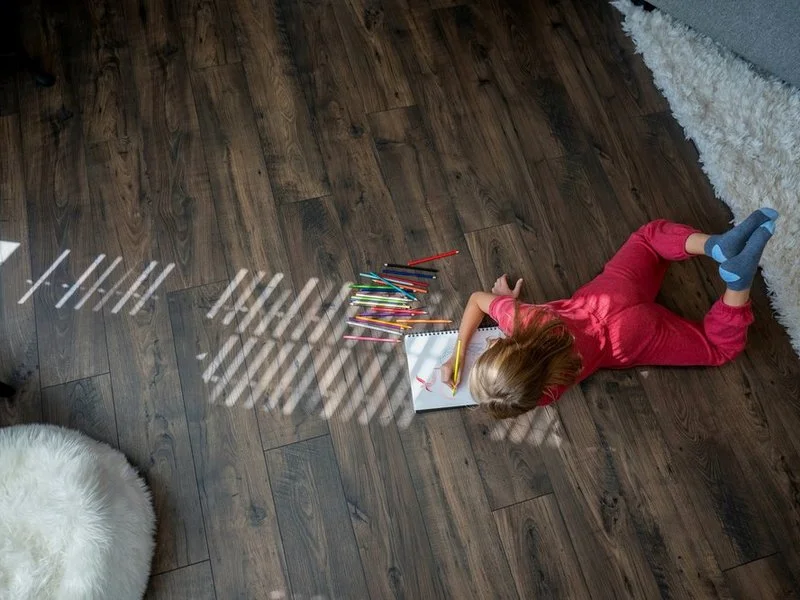 A child drawing on warm dark hardwood flooring in a Grand Rapids area living room