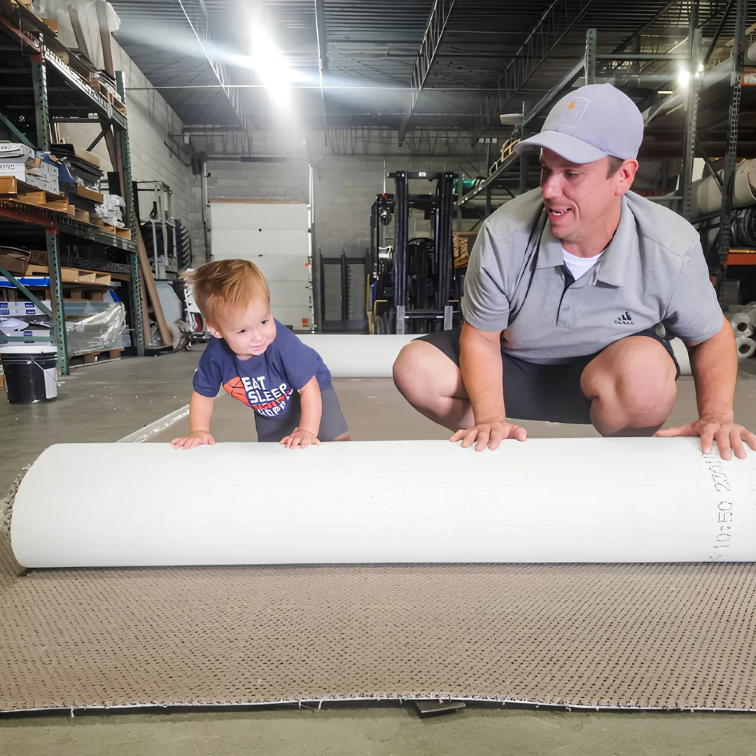 Jamie VanTuinen unrolling carpet padding alongside his son in the Absolute Flooring warehouse